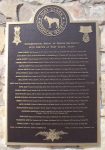 A bronze plaque mounted on a stone wall, featuring text commemorating an historical event or figure, with decorative elements at the top.