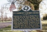 Historical marker honoring Pvt. Robert L. 'Bobby' Henry for his actions in World War II, with an American flag in the background.