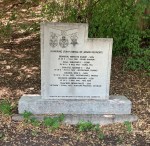 A stone memorial marker displaying honors and names, surrounded by greenery.