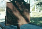 Historical marker commemorating Ovid Wellesford Smith, located in a cemetery with trees in the background.