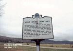 A historical marker for Wolf River Cemetery, with a grey overcast sky in the background.
