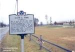 A historical marker dedicated to Alvin C. York, located on the side of a road, with a grassy field in the background and a cloudy sky.